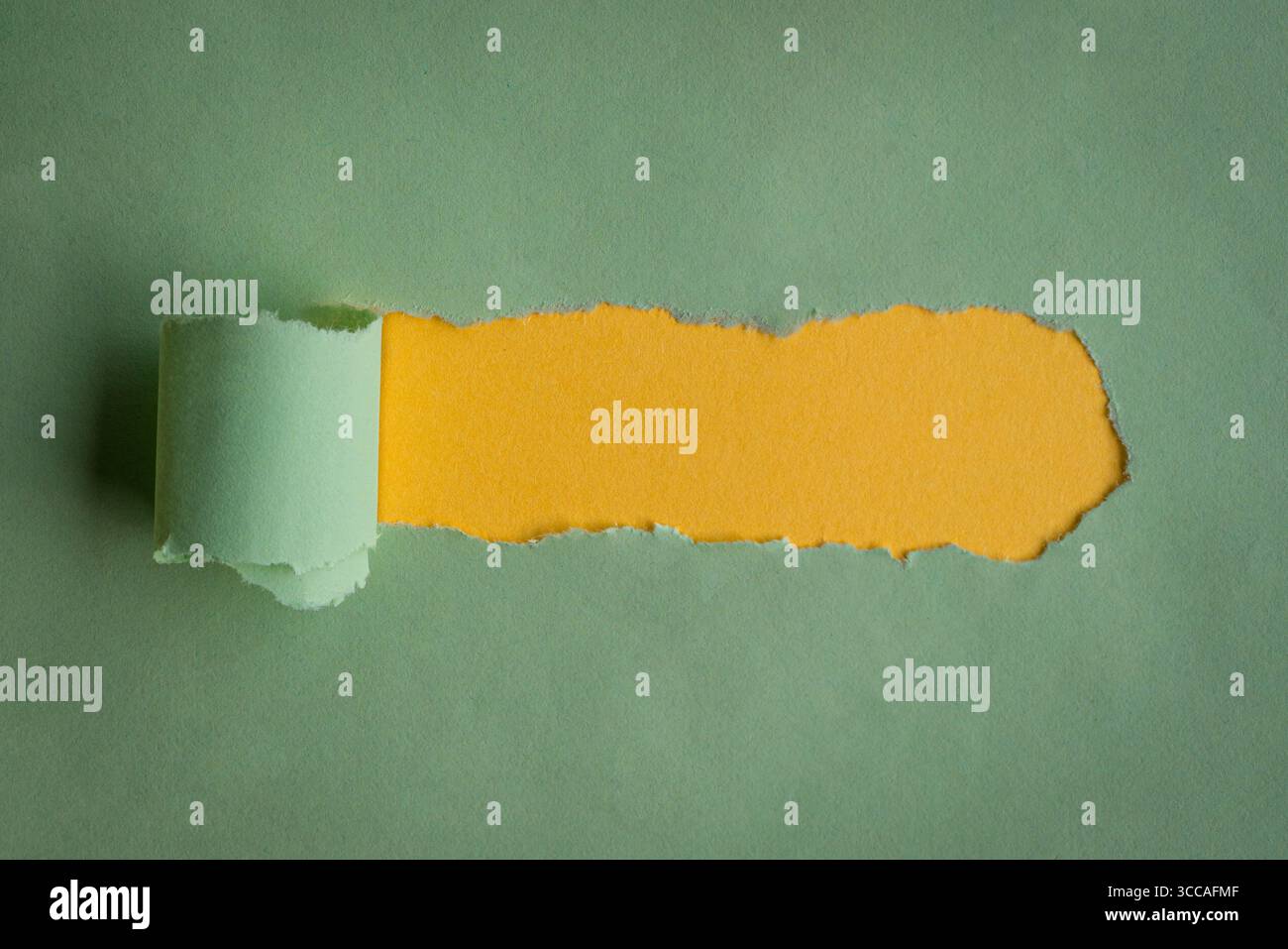 Hole ripped in green paper on yellow background. Copy space. Stock Photo