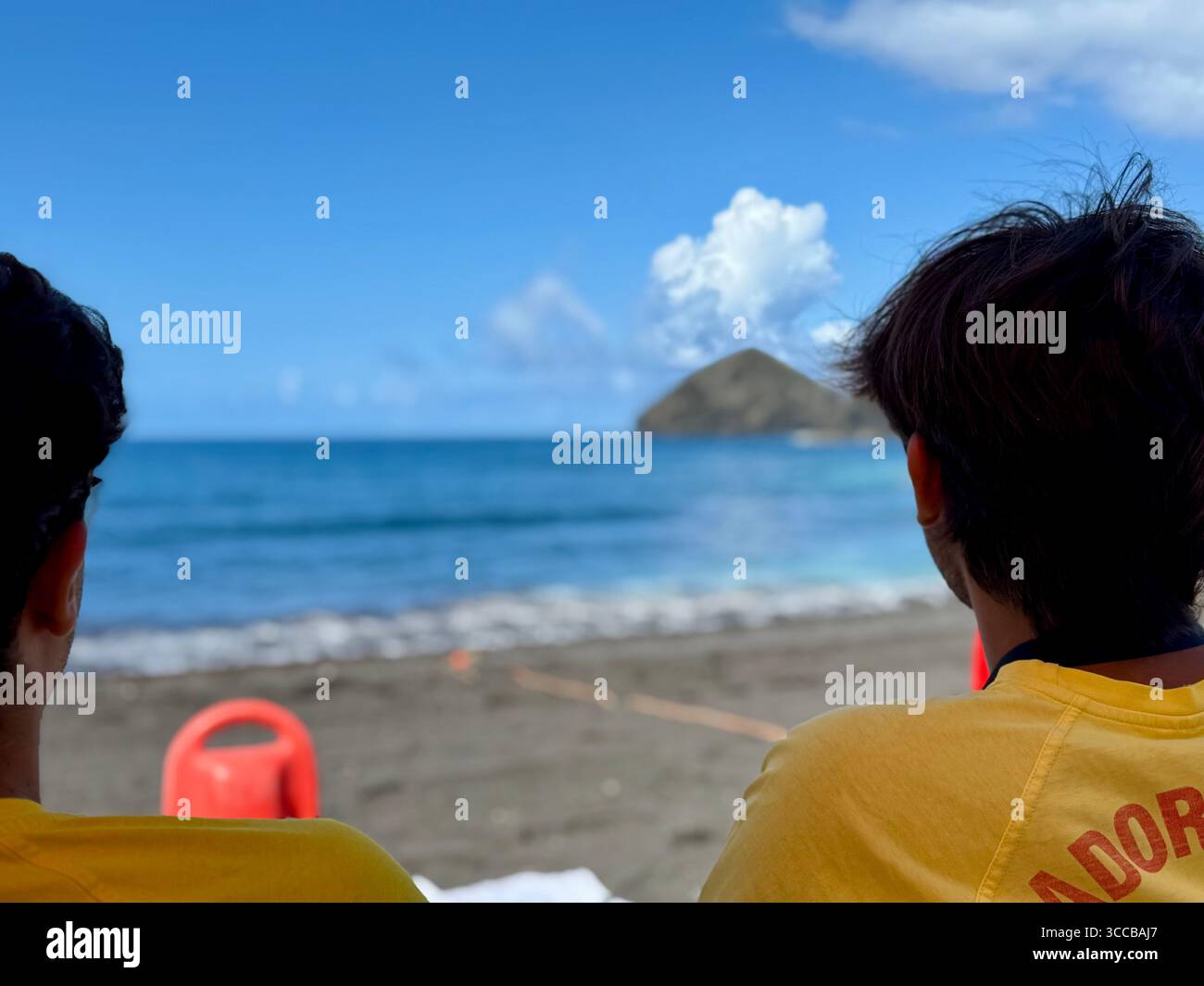 Two lifeguards watching the sea from a beach outpost at Mosteiros Beach, Azores, Portugal, with volcanic islets in the distance. - Smartphone Captured Stock Image