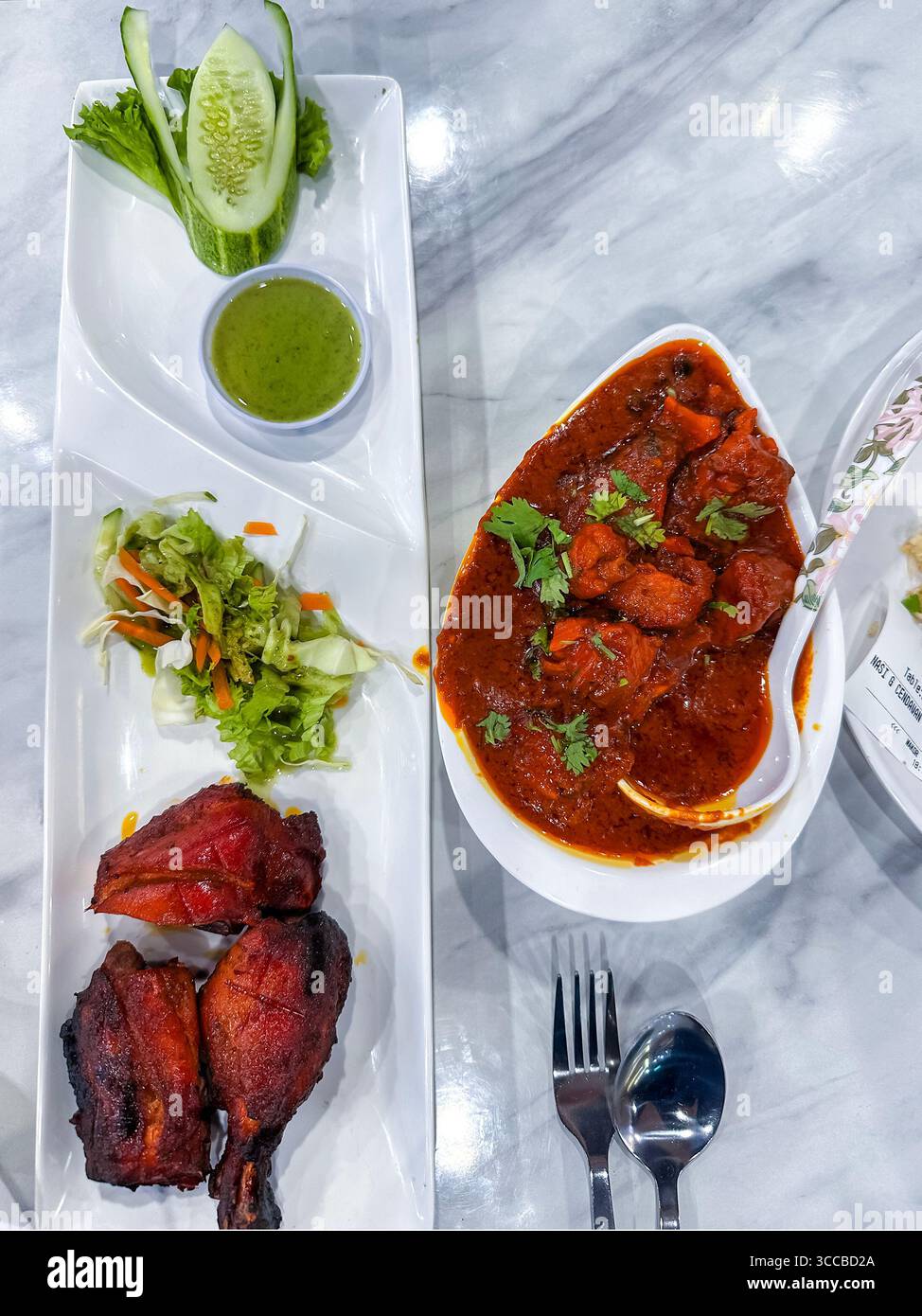 Delicious Indian curry meal featuring tandoori chicken, spicy curry, green chutney, and fresh salad on a marble restaurant table kuala lumpur malaysia - Smartphone Captured Stock Image
