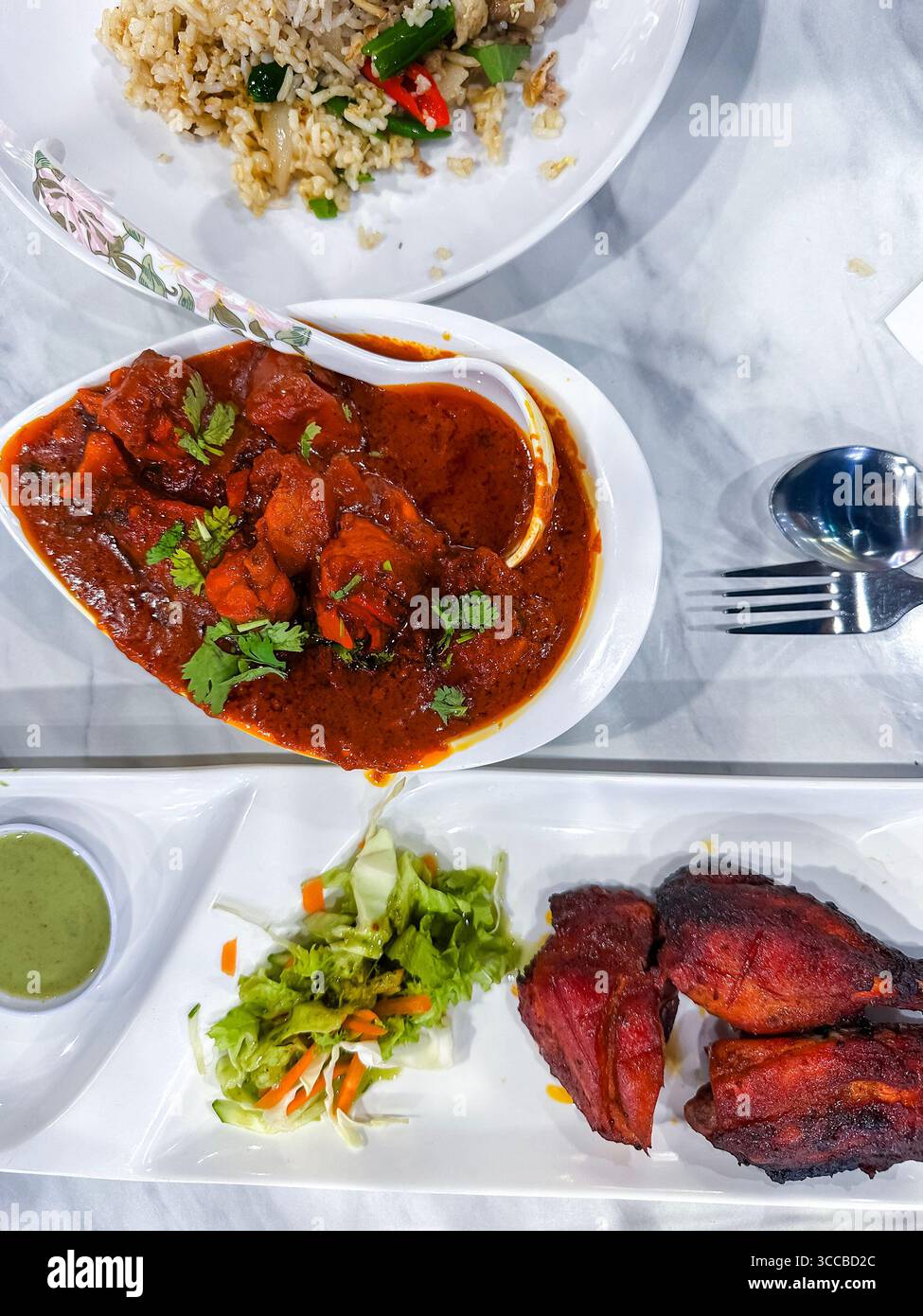 Delicious Indian curry meal featuring tandoori chicken, spicy curry, green chutney, and fresh salad on a marble restaurant table kuala lumpur malaysia - Smartphone Captured Stock Image
