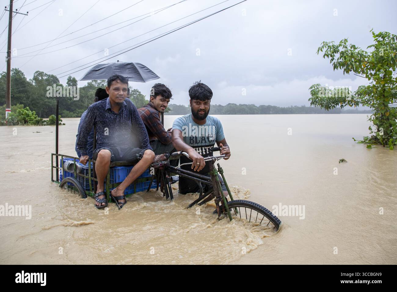 Satkania, Bangladesh - 09 August 2023: View of resilient figures navigating the floodwaters in a rickshaw, their faces reflecting the challenging conditions under a grey, overcast sky. Stock Photo