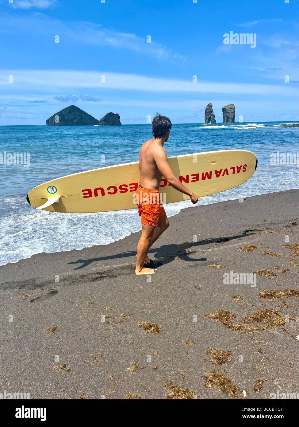Lifeguard on duty at Mosteiros Beach, São Miguel Island, Azores, Portugal, walking across the sand with a rescue board. - Smartphone Captured Stock Image