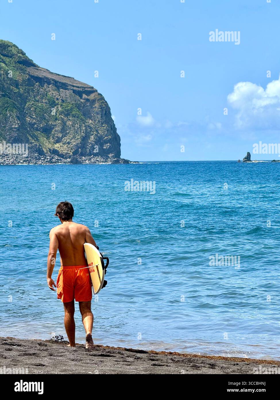 Lifeguard on duty at Mosteiros Beach, São Miguel Island, Azores, Portugal, walking across the sand with a rescue board. - Smartphone Captured Stock Image