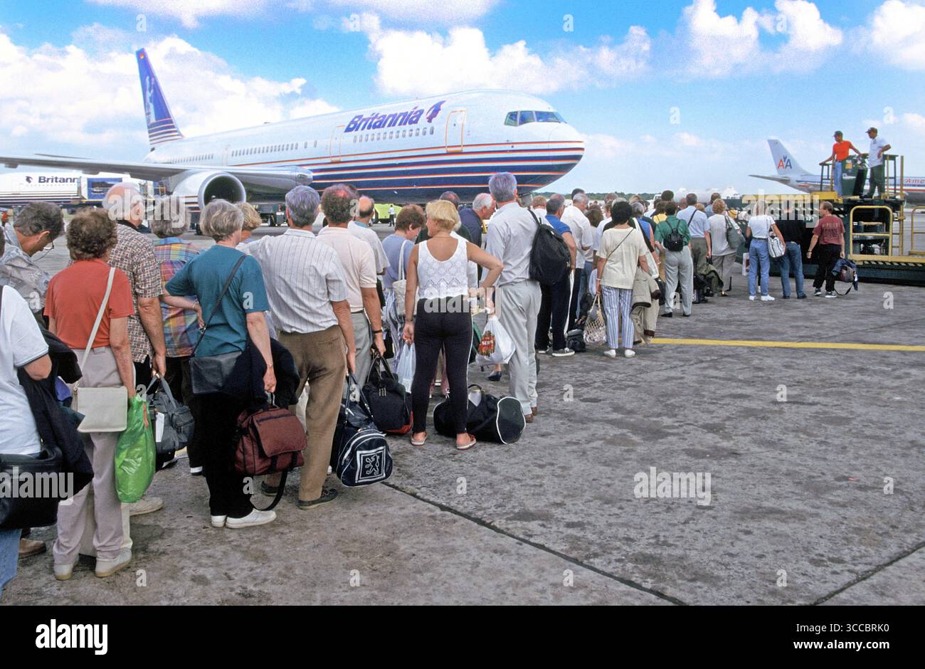 Britannia Thomson Boeing jet airliner provides  a backdrop to returning home holiday travellers in1998 archive back view of passengers in 90s travel fashions with hand luggage queuing to board jet airliner for non stop return flight to Gatwick London UK departing from this 90s Santo Domingo Airport in the Dominican Republic watched over by ground crew a lifestyle  archival image of the way we were back then in 1990s Stock Photo