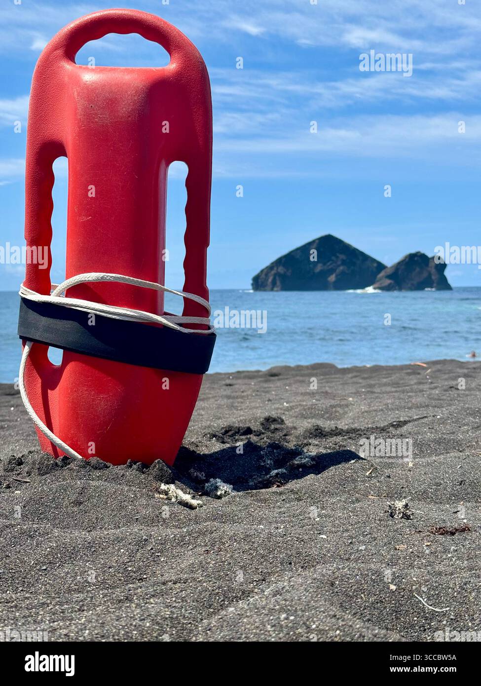 Red torpedo float stuck in black sand at Mosteiros Beach, Azores, Portugal, with volcanic islets in the background. - Smartphone Captured Stock Image