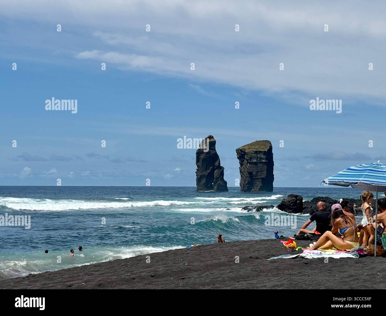People sunbathing and swimming at Mosteiros Beach, Azores, with volcanic rock formations in the Atlantic Ocean. - Smartphone Captured Stock Image