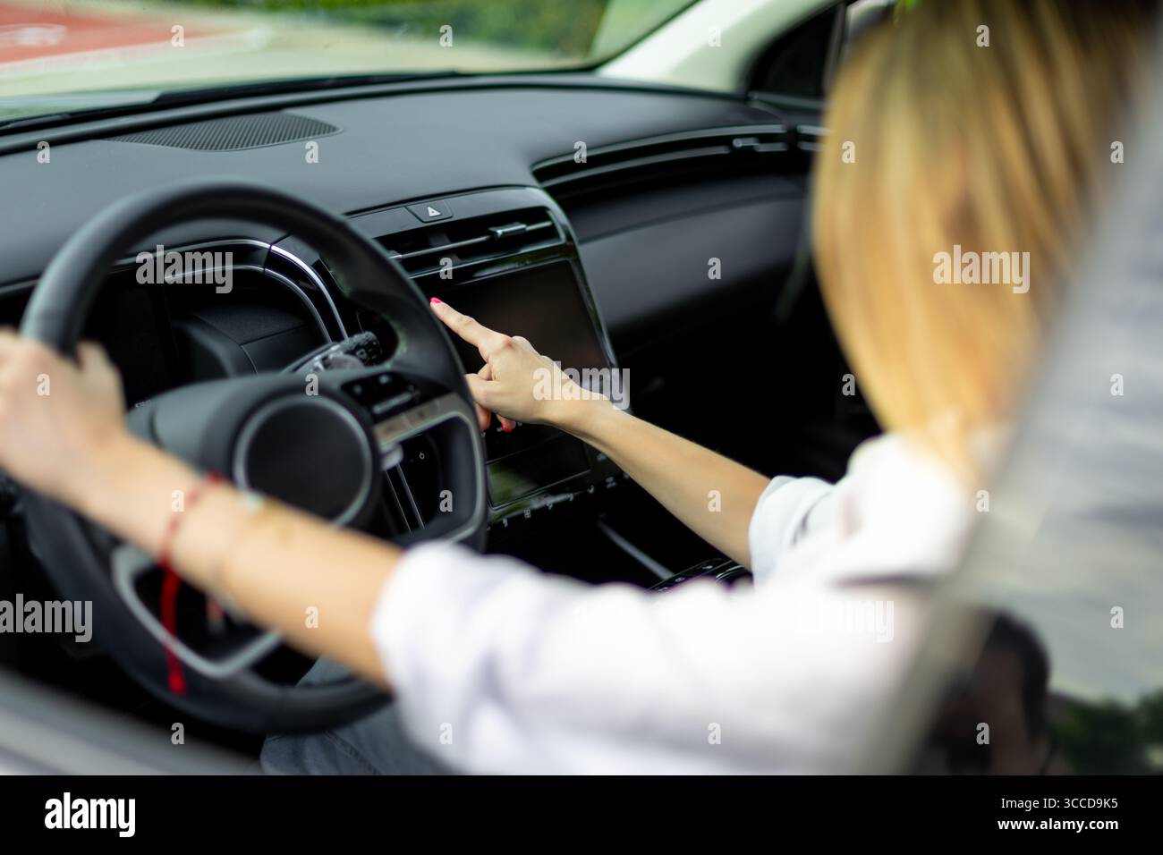 Businesswoman driving a modern car and using the touchscreen navigation system while holding the steering wheel Stock Photo