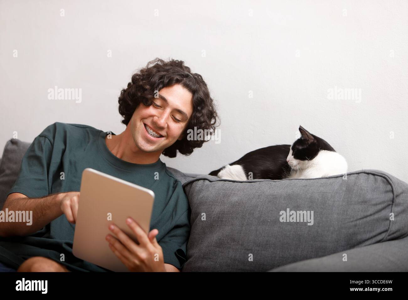 Smiling man using tablet on sofa with a resting cat beside him Stock Photo