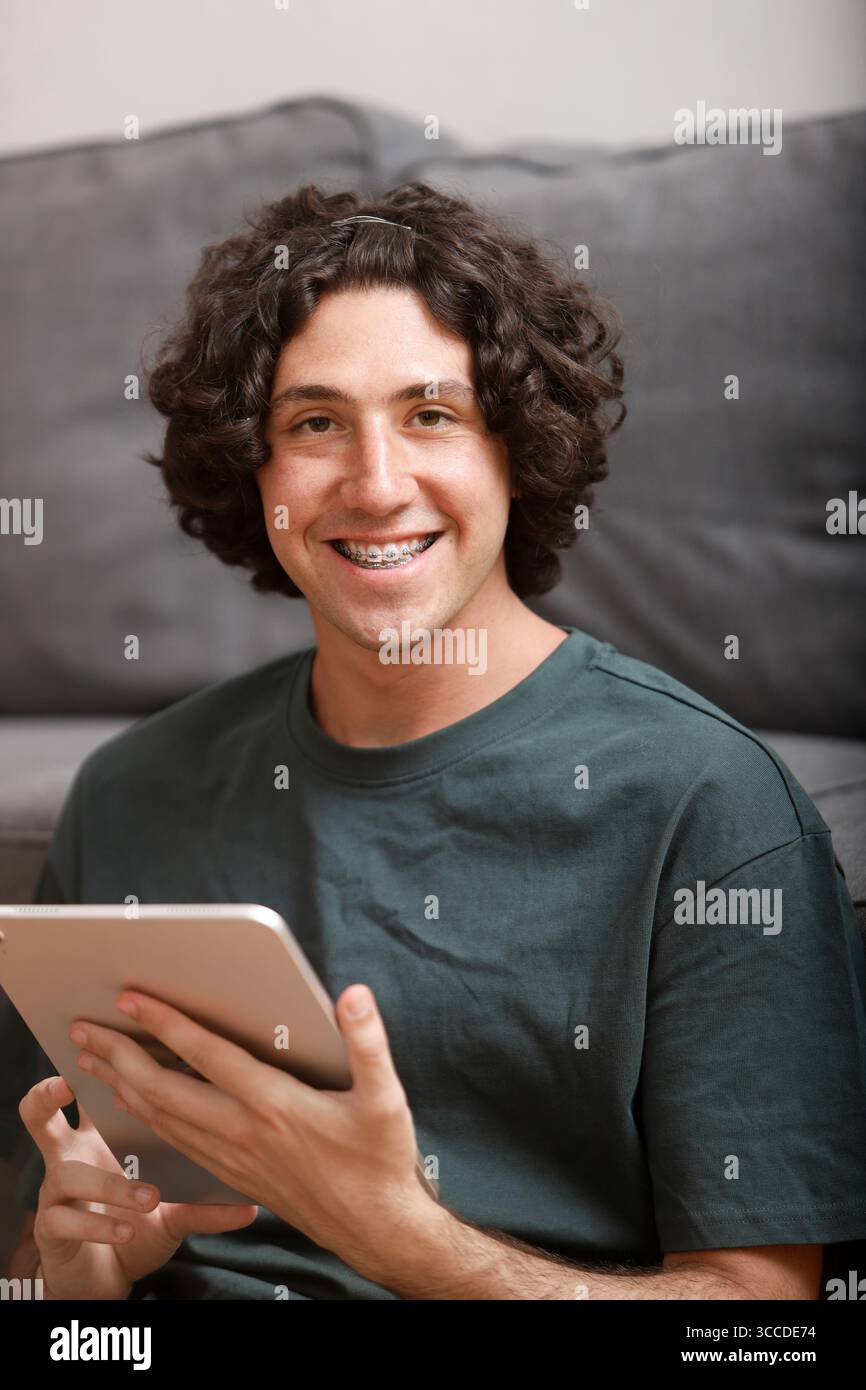 Happy young man with braces using digital tablet, enjoying online activity or working remotely Stock Photo