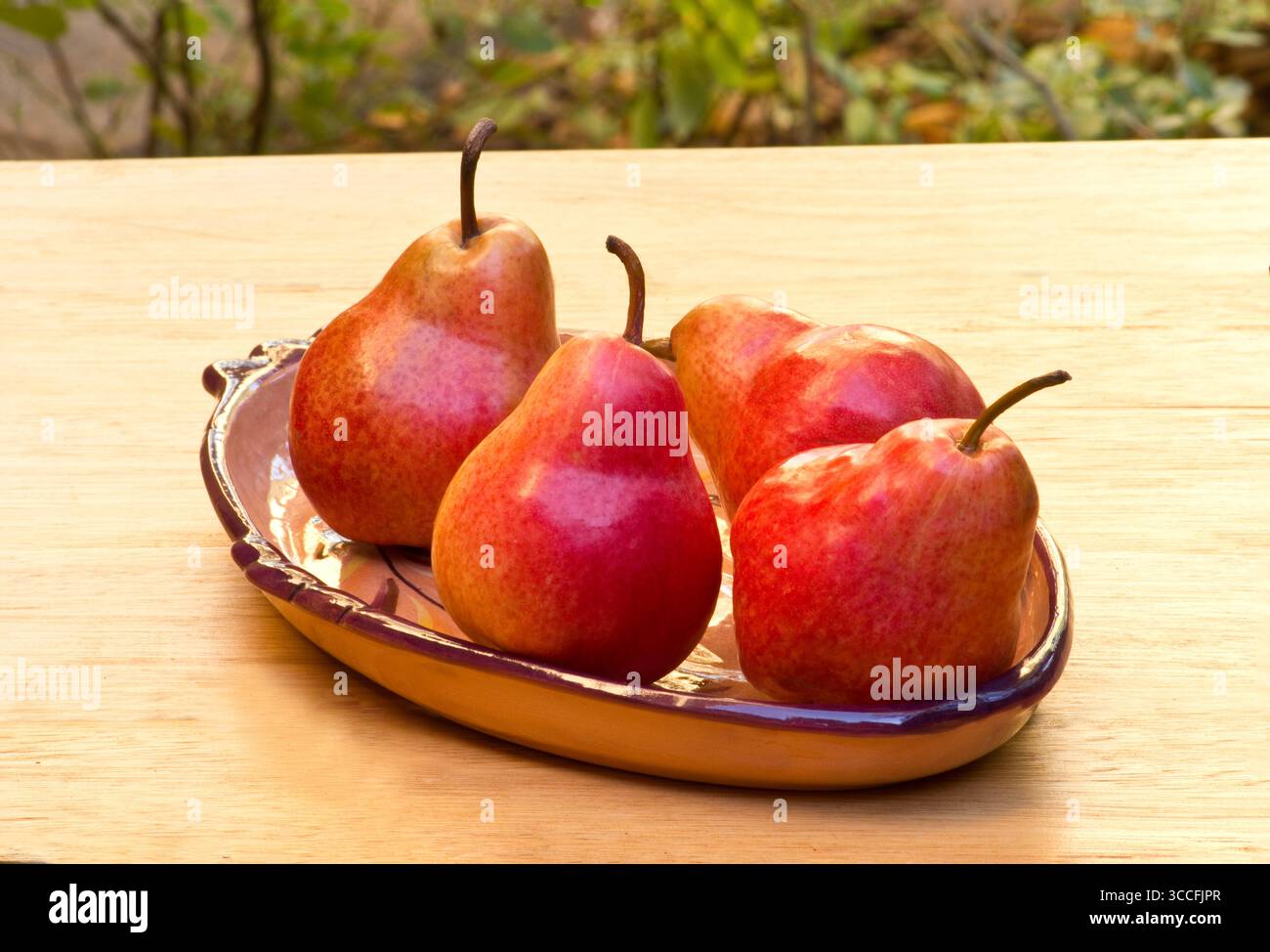 Red pears on a ceramic bowl on a wooden table Stock Photo