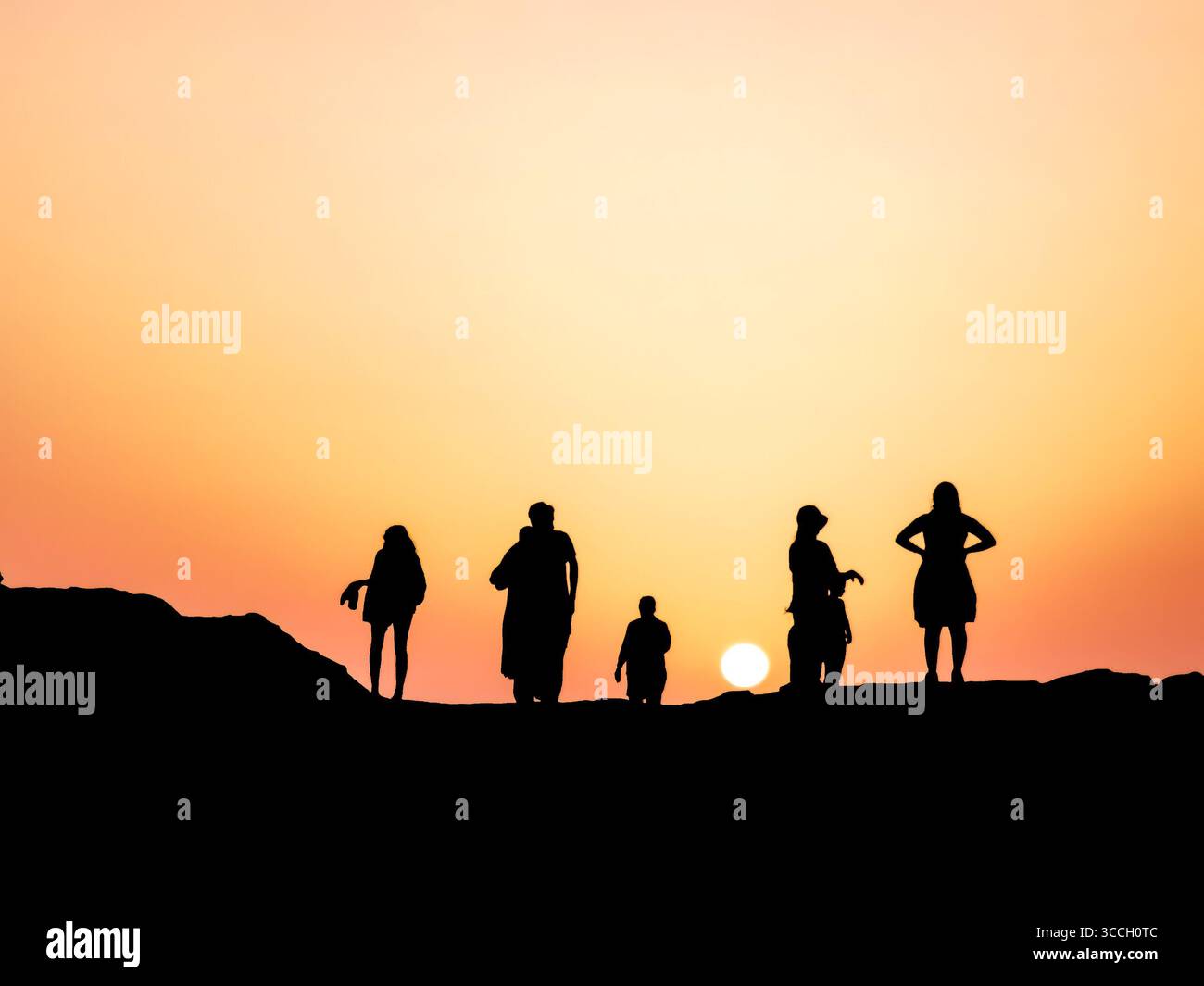 A group of people walks on the rocky beach of Cape Zebib, Bizerte, Tunisia. The sun, low on the horizon, casts warm light, creating a peaceful scene. - Smartphone Captured Stock Image