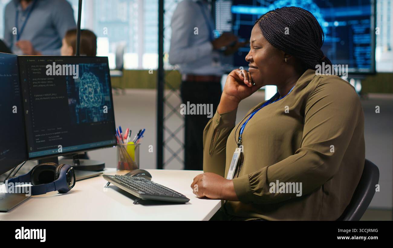 Jolly female programmer at office desk pleased after developing application using machine learning automation. Joyous employee satisfied after debugging applications using neural networks, camera A Stock Photo