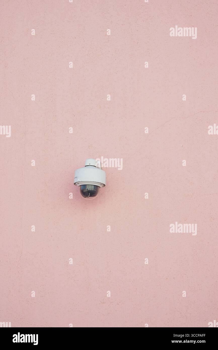 Security camera mounted on a pink wall in bright daylight Stock Photo