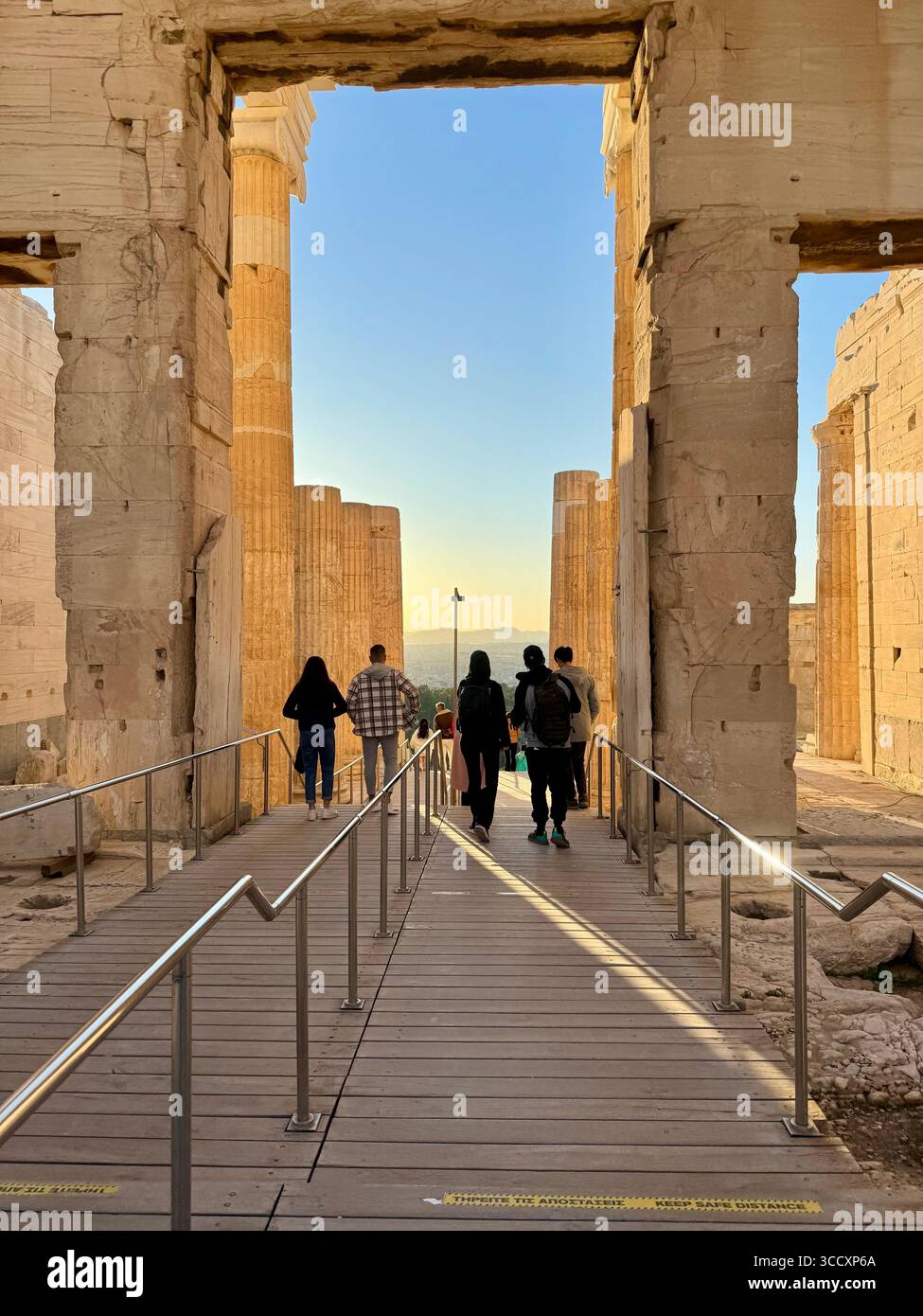 Golden hour sunset at the entrance of the Acropolis complex (Acrópole Propileia) in Athens, Greece, with tourists walking down the stairs. - Smartphone Captured Stock Image