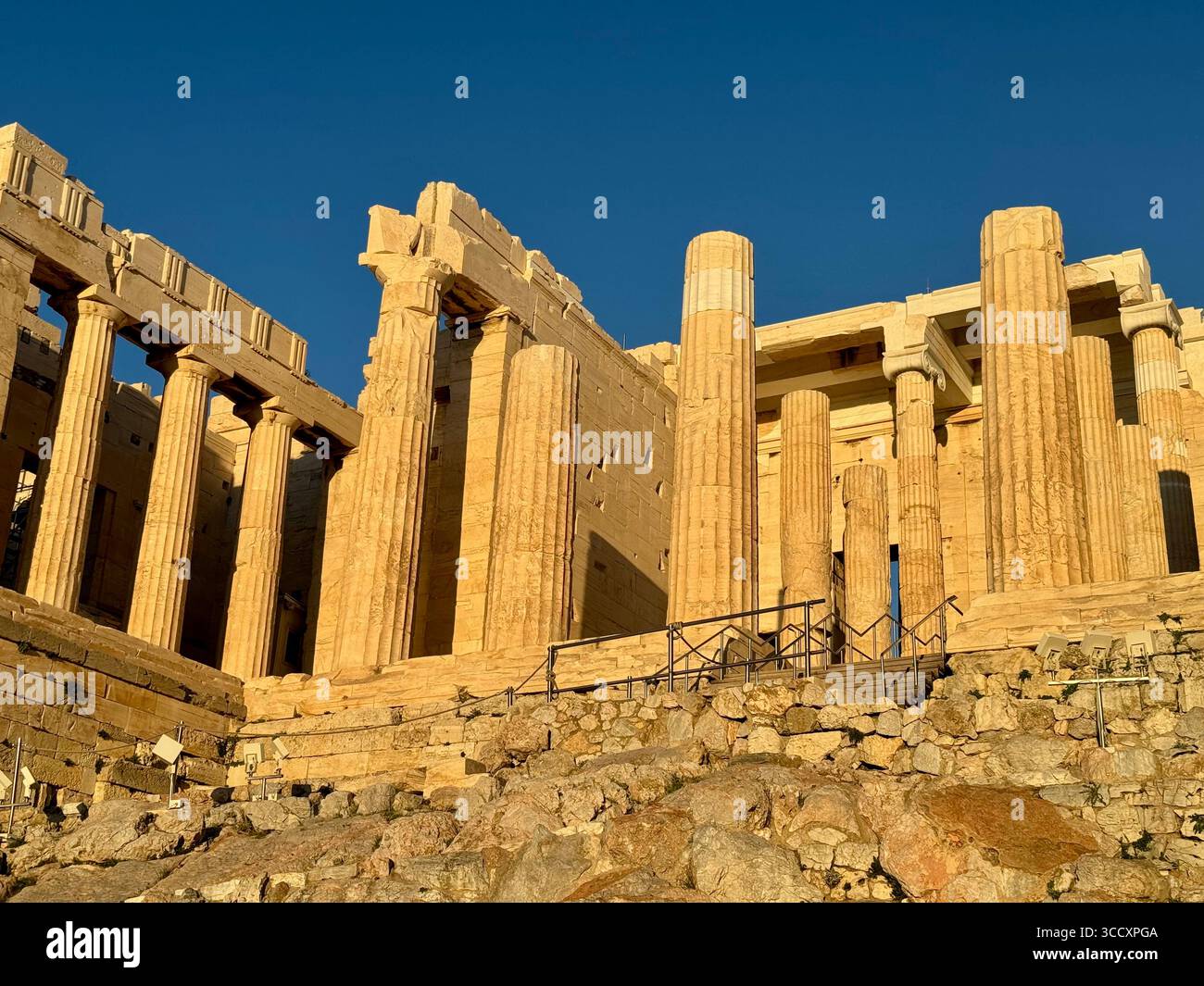 Golden hour sunset at the entrance of the Acropolis complex (Acrópole Propileia) in Athens, Greece, with tourists walking down the stairs. - Smartphone Captured Stock Image