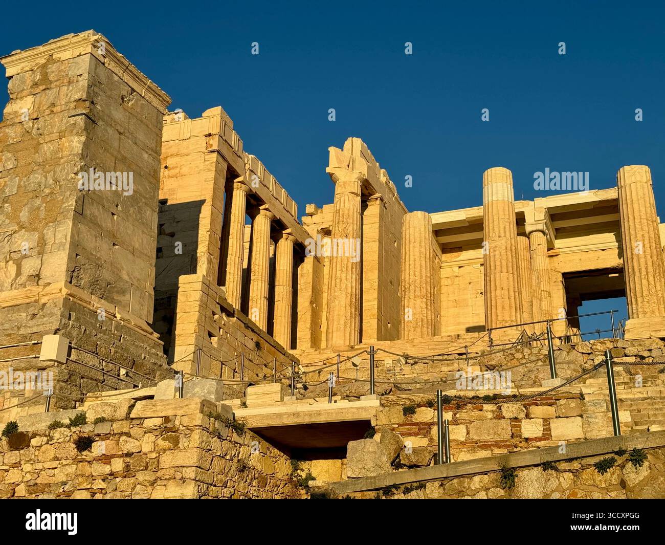 Golden hour sunset at the entrance of the Acropolis complex (Acrópole Propileia) in Athens, Greece, with tourists walking down the stairs. - Smartphone Captured Stock Image
