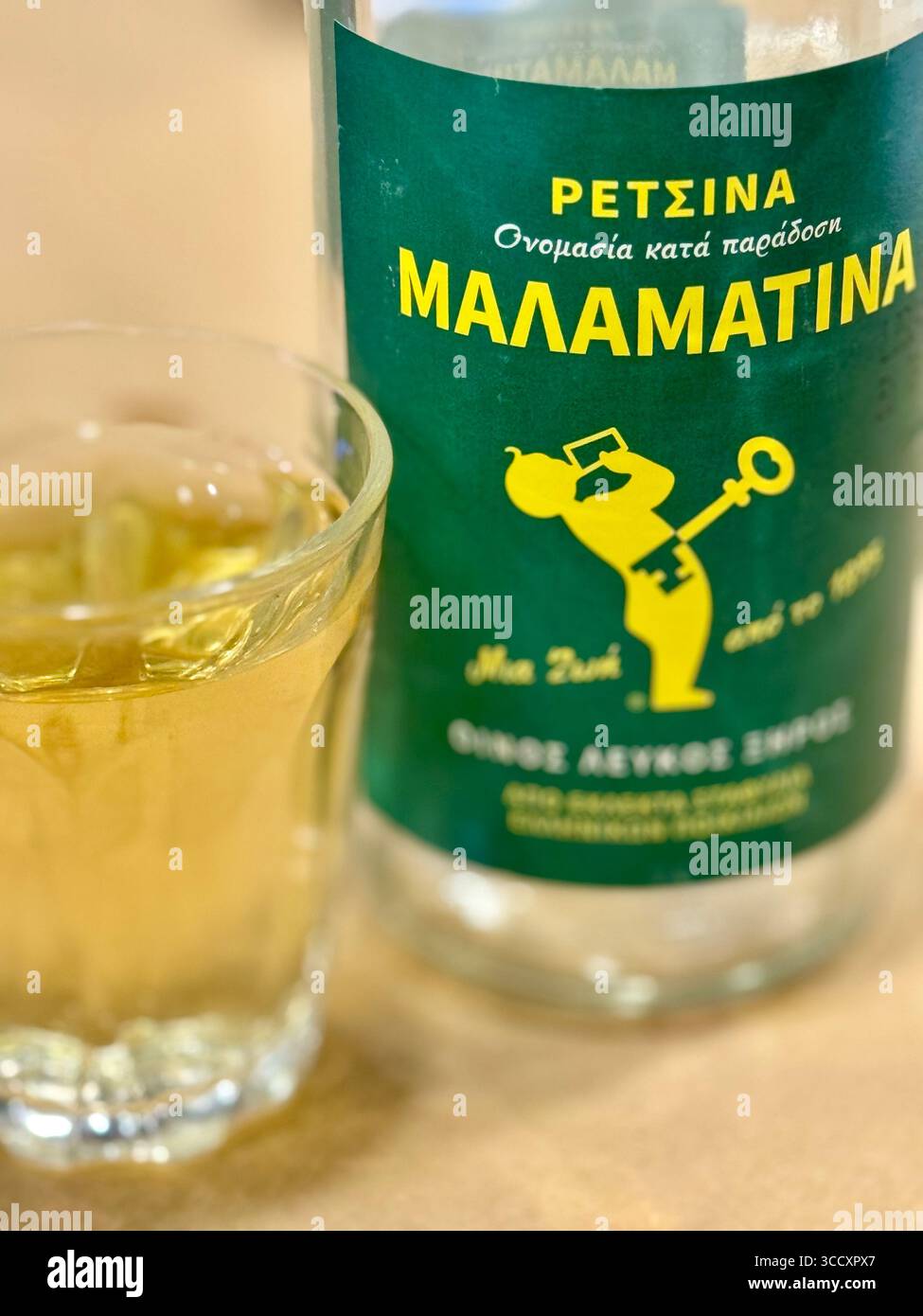 A bottle of Malamatina Retsina wine with a glass filled with the traditional Greek beverage. - Smartphone Captured Stock Image