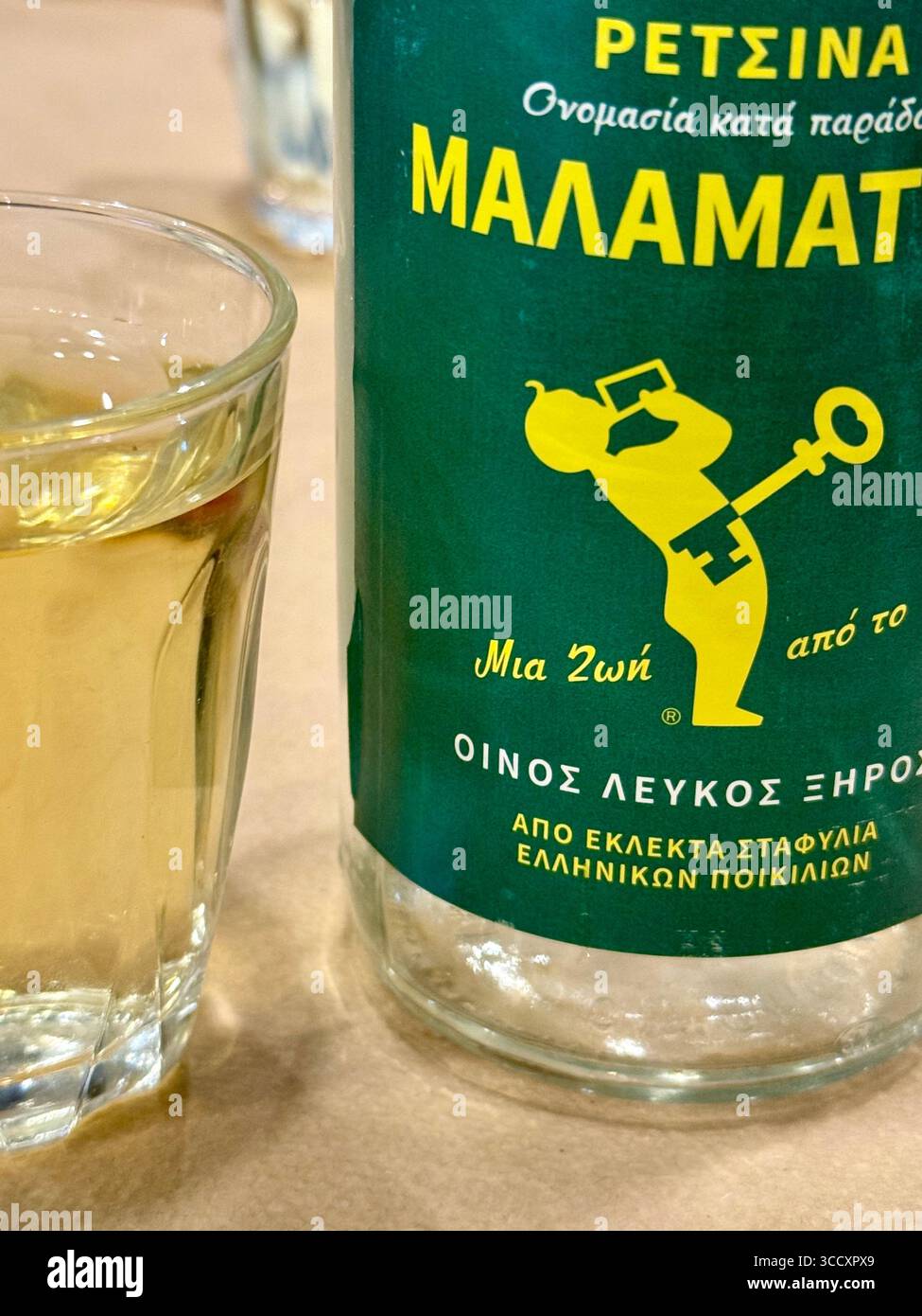 A bottle of Malamatina Retsina wine with a glass filled with the traditional Greek beverage. - Smartphone Captured Stock Image