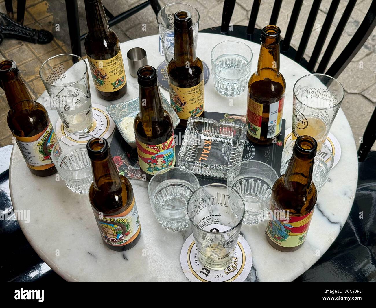 Greek beer bottles and empty glasses on a marble table outdoors. - Smartphone Captured Stock Image