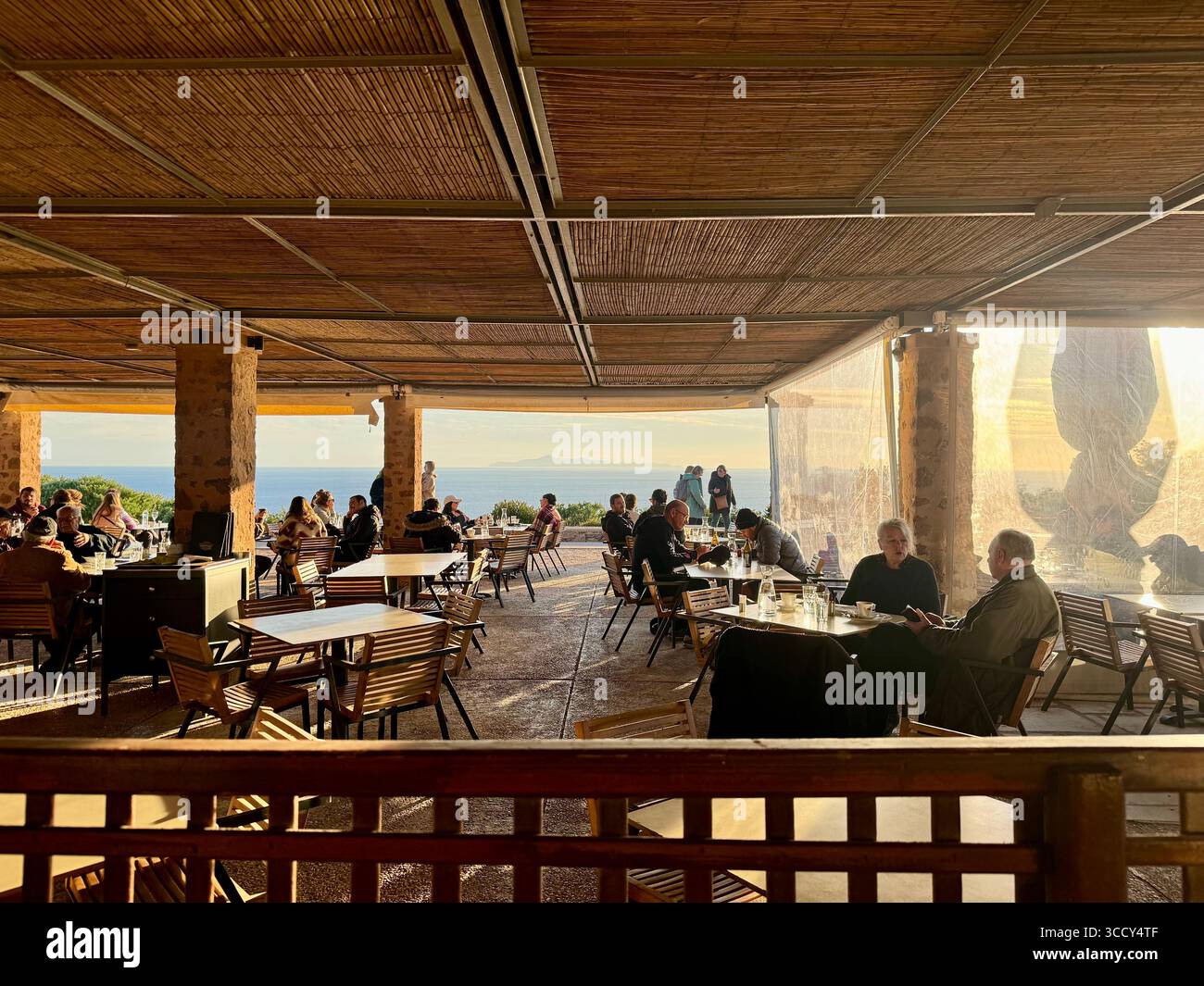 People dining on a scenic terrace with a view of Agios Georgios Island at sunset, Cape Sounion, Greece. - Smartphone Captured Stock Image