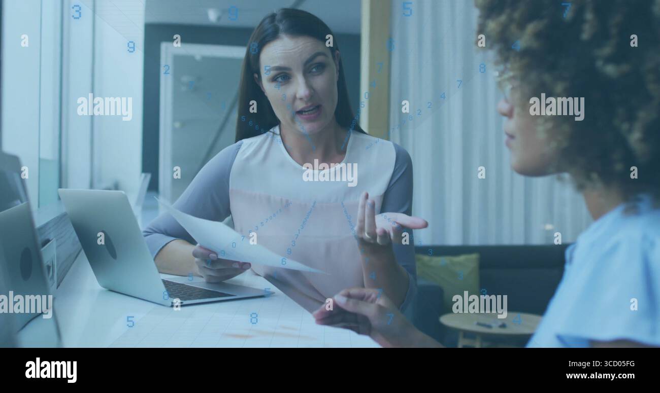 Discussing documents two women wearing blouses and gesturing at conference room, with laptop Stock Photo