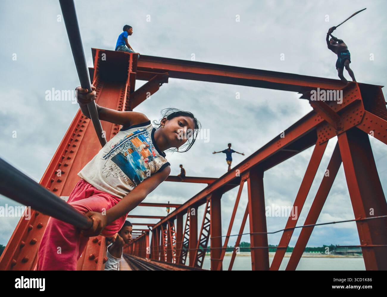 Bogura, Bangladesh - 19 October 2017: View of children playfully balancing and climbing on the vibrant red steel structure against a cloudy sky. Stock Photo
