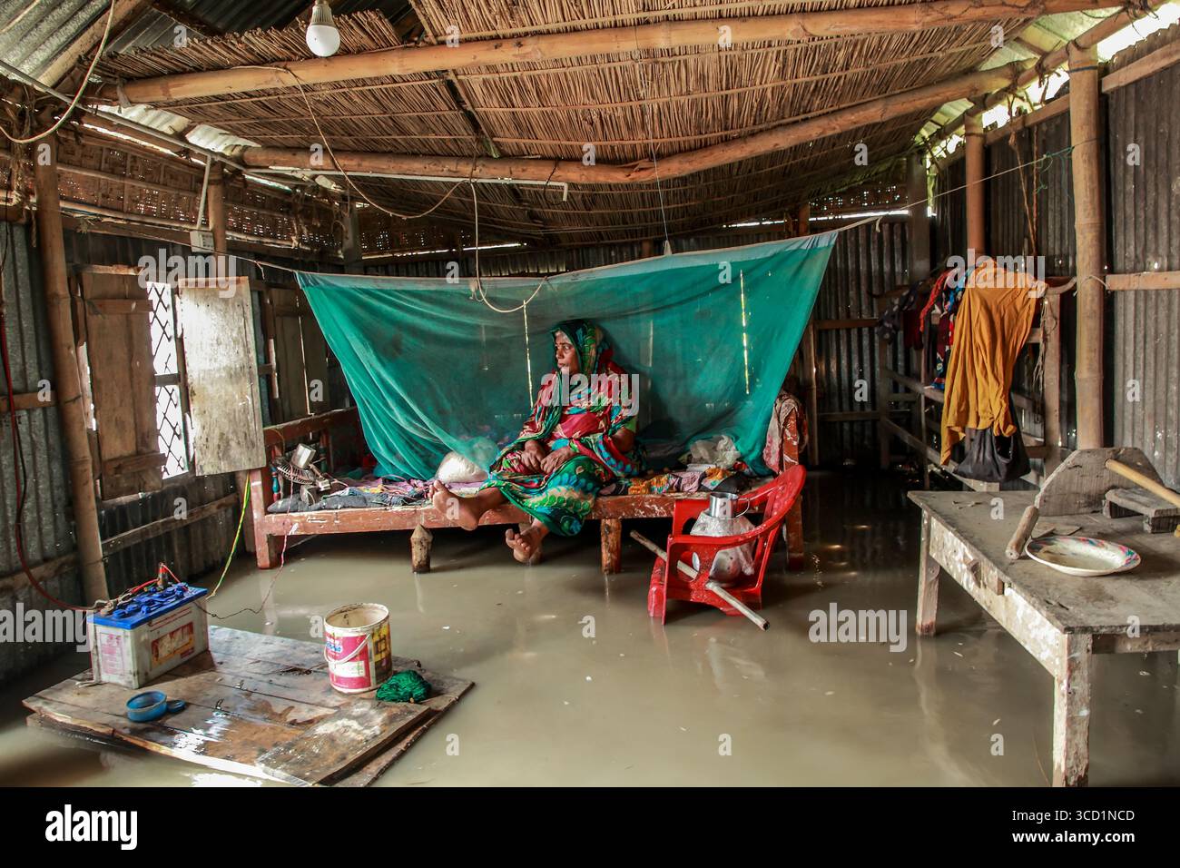 Kurigram, Bangladesh - 21 June 2022: View of a woman amid floodwaters inside her home, a poignant tableau of resilience under a thatched roof. Stock Photo