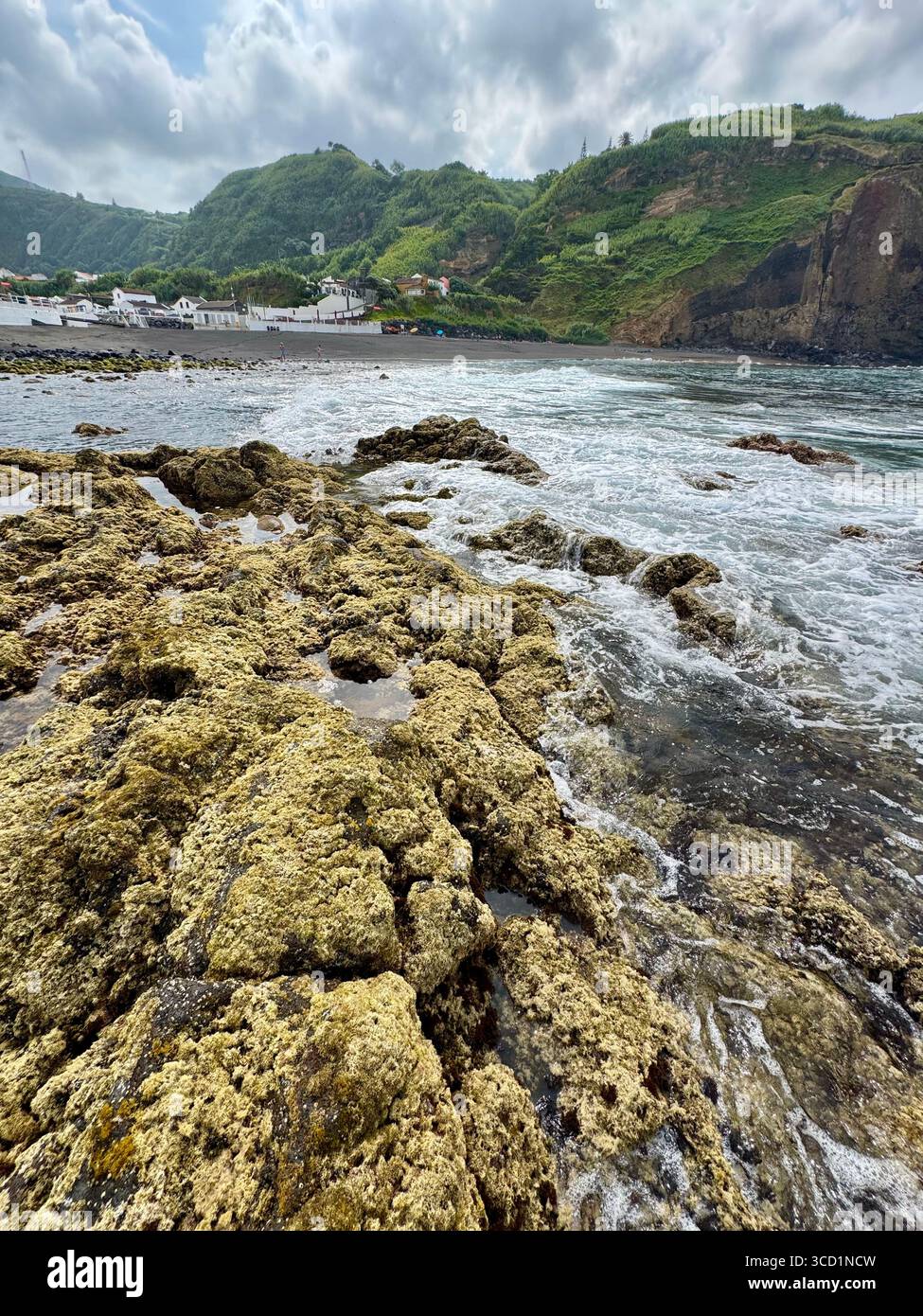 Low tide at Mosteiros Beach with rocky shoreline, village, and mountains in the background. - Smartphone Captured Stock Image