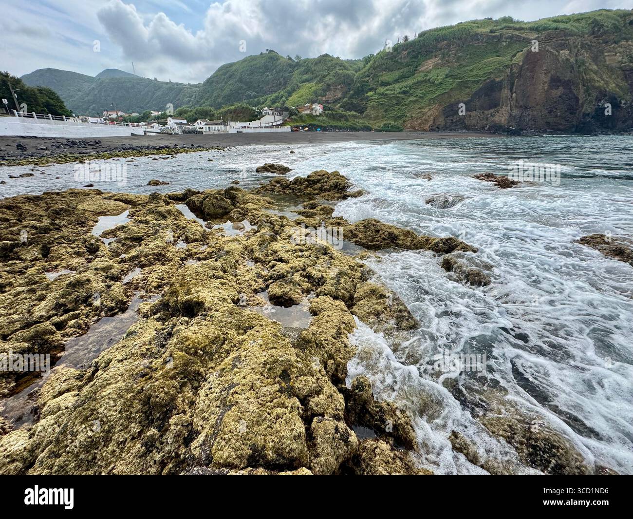 Low tide at Mosteiros Beach with rocky shoreline, village, and mountains in the background. - Smartphone Captured Stock Image