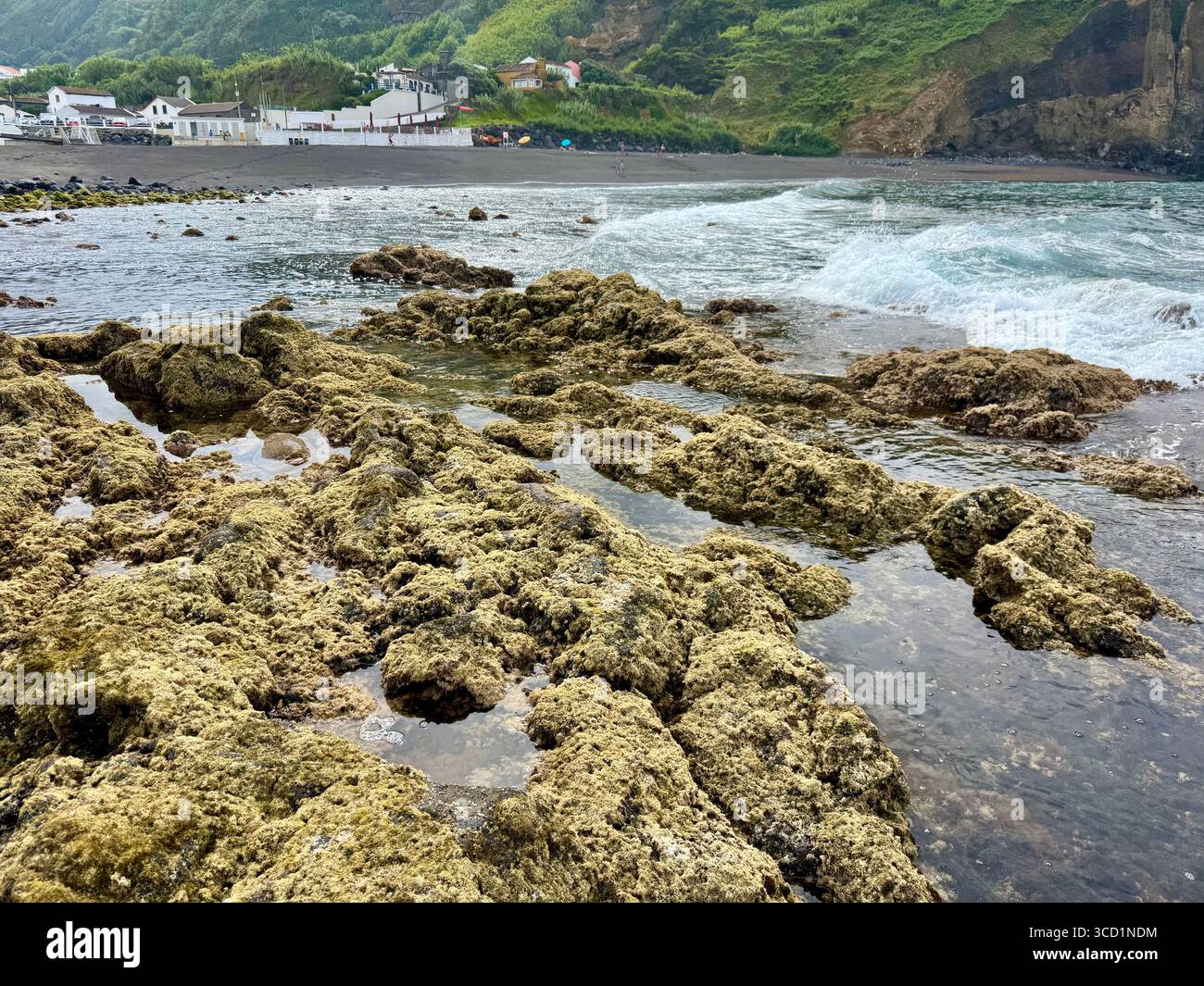 Low tide at Mosteiros Beach with rocky shoreline, village, and mountains in the background. - Smartphone Captured Stock Image