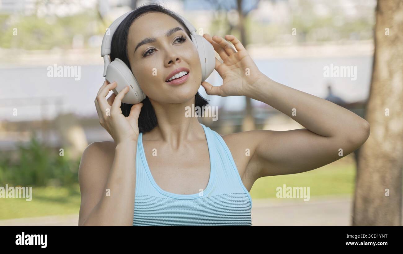 Fitness-focused female enjoying a workout in the park with headphones, feeling energized and healthy Stock Photo