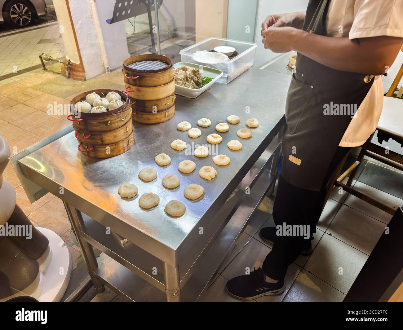 Person preparing dough for traditional Jiaozi dumplings in a kitchen with stacked bamboo steamers and a table filled with ingredients Penang Malaysia - Smartphone Captured Stock Image