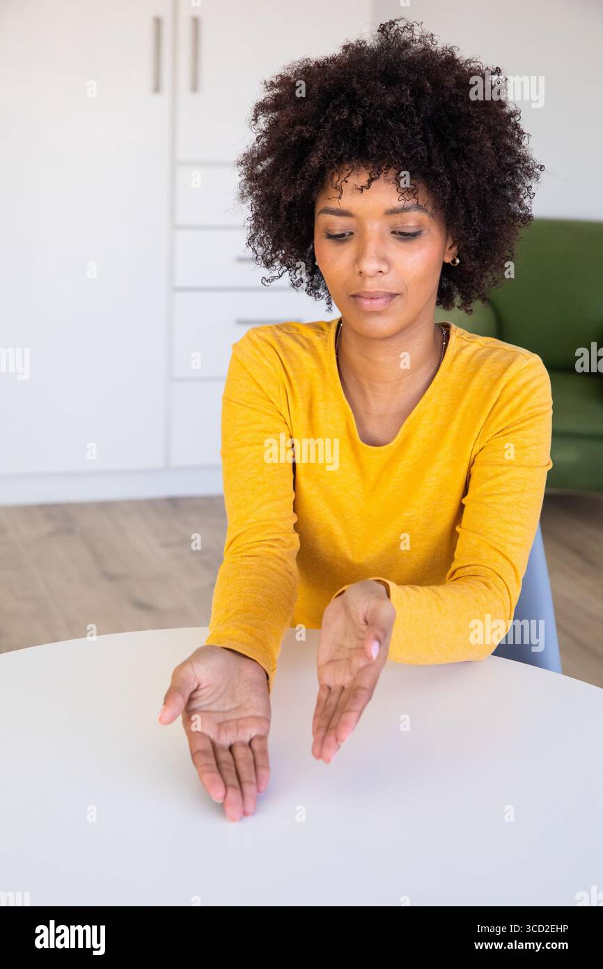 African American woman presenting palms above round table in modern living area with green sofa Stock Photo