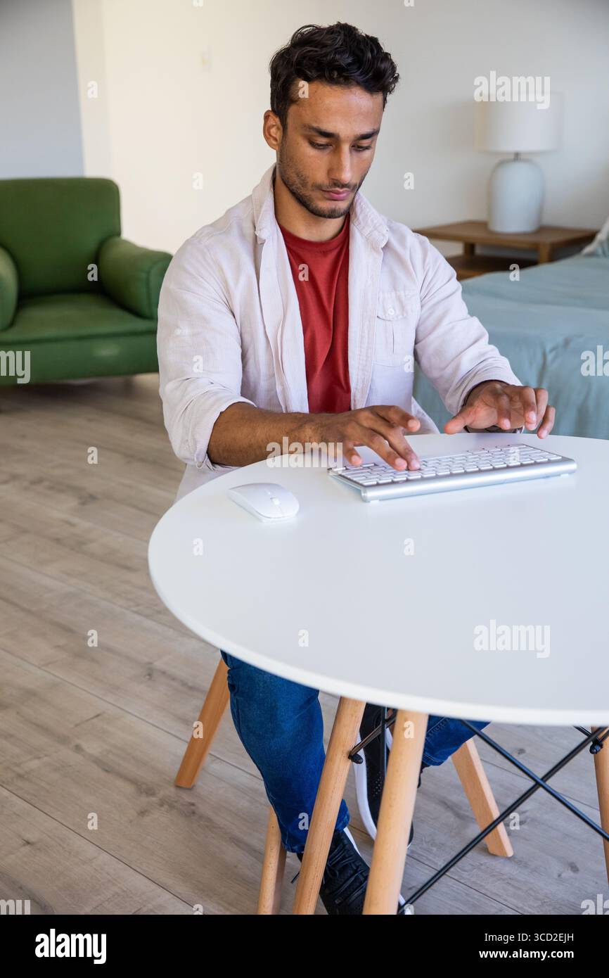 Man typing on wireless keyboard at small round table in bedroom living area with wireless mouse Stock Photo
