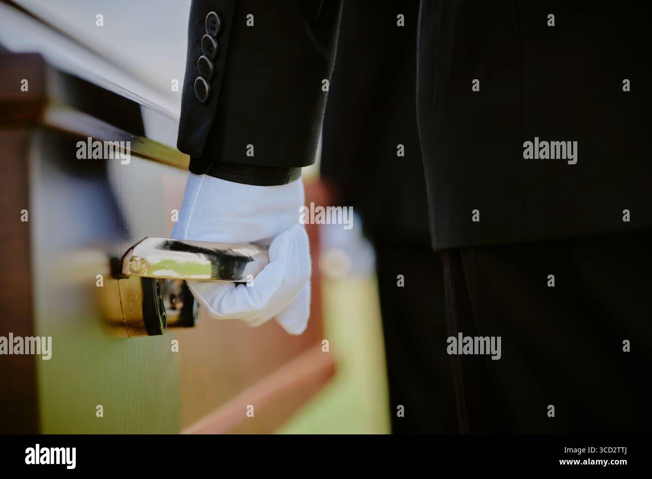 Caucasian middle aged man wearing suit and glove holding wooden casket handle during funeral ceremony outdoors, close up on hand and arm, solemn moment of mourning Stock Photo
