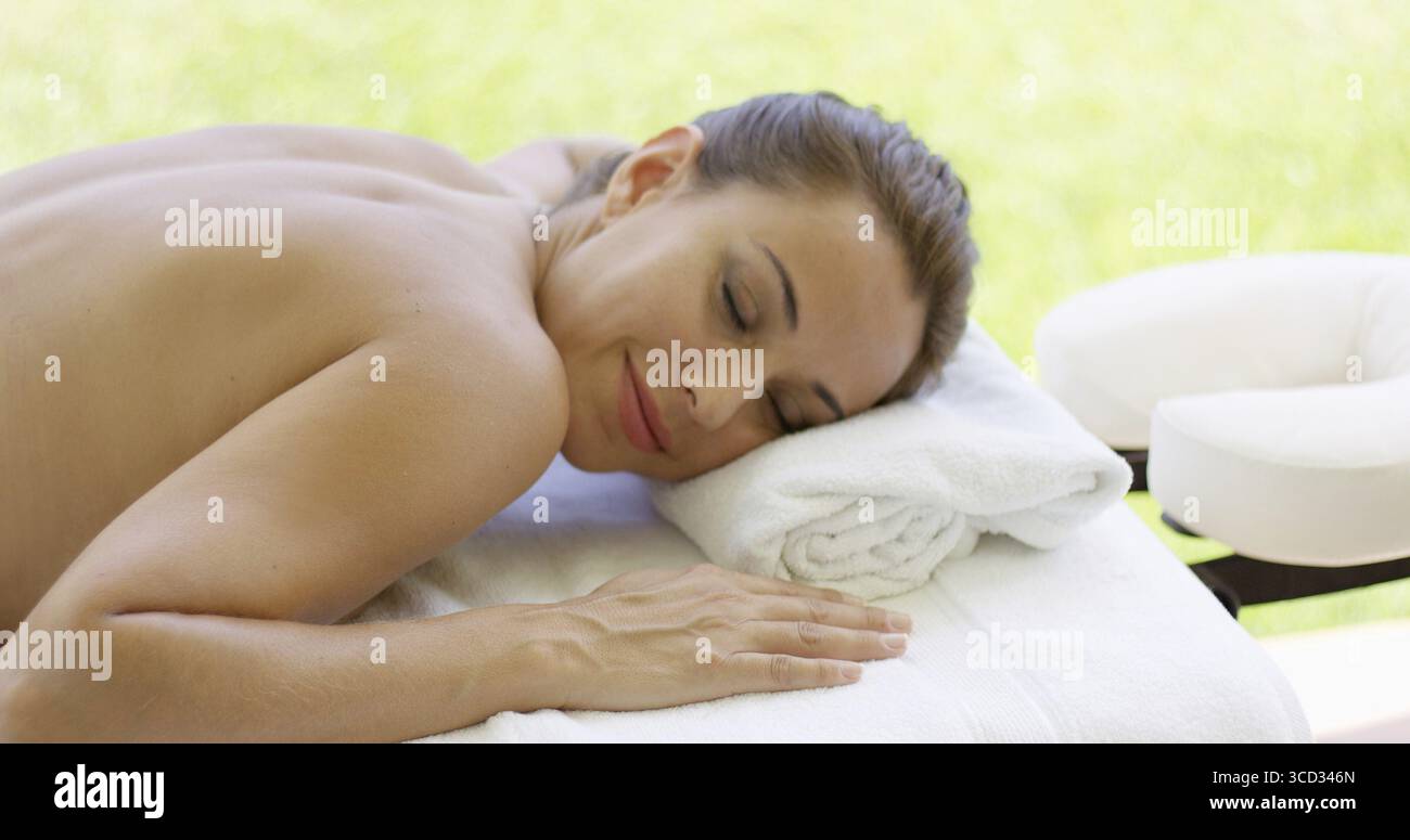 Woman smiles at camera while at spa on outdoor massage table on sunny afternoon Stock Photo