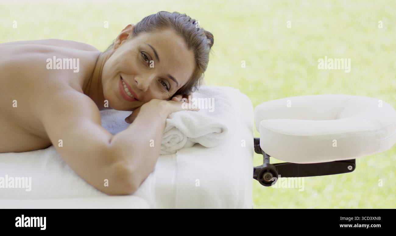 Woman smiles at camera while at spa on outdoor massage table on sunny afternoon Stock Photo