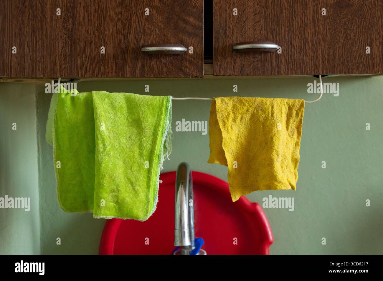 Two kitchen rags, green and yellow, hang on a rope above the sink under ...