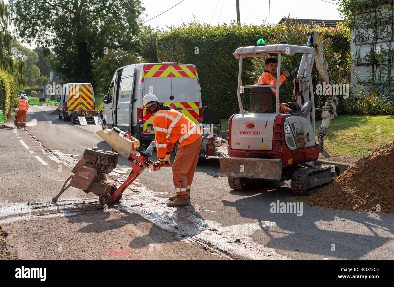 Hampshire England UK 07.08.2025. Workman using a road cutting saw machine to cut through road surface before trenching work. Stock Photo