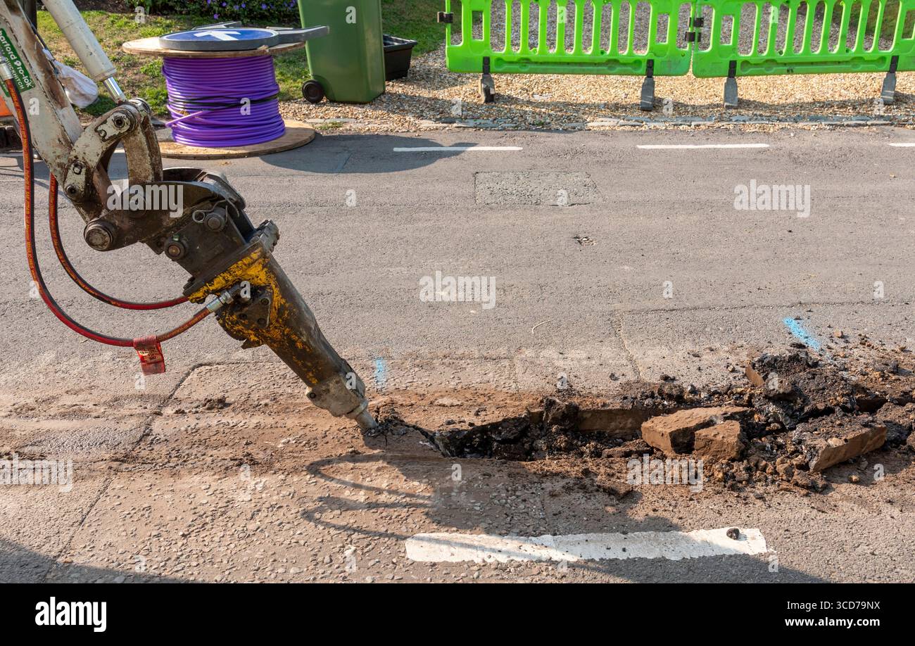 Hampshire England UK.07.08.2025. Hydraulic breaker attachment breaking road surface before trench digging operation for full fibre network cable Stock Photo