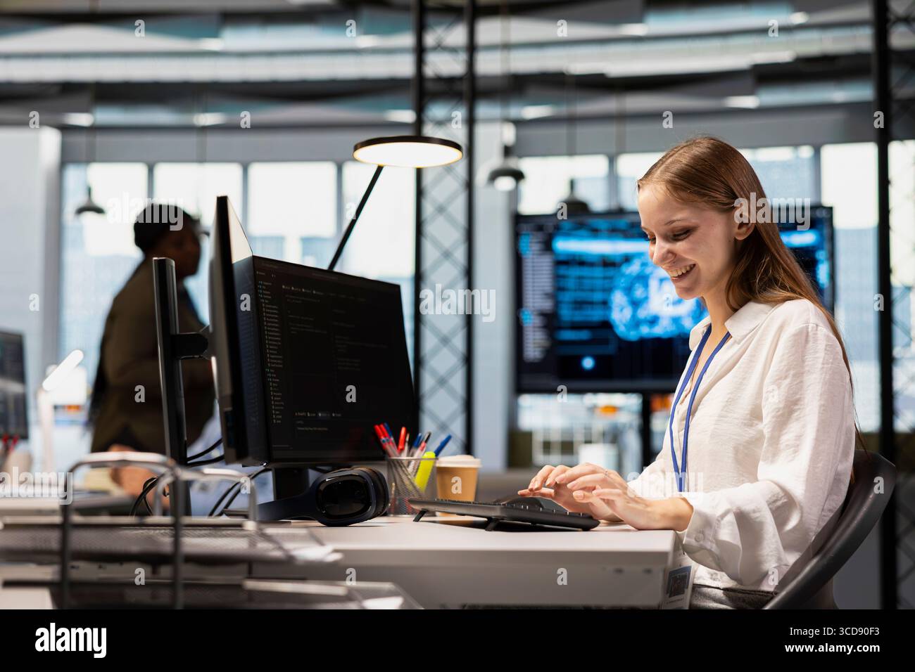 Cheerful junior dev writing code, developing machine learning APIs. Happy young female engineer working in office, troubleshooting software errors using artificial intelligence tech Stock Photo