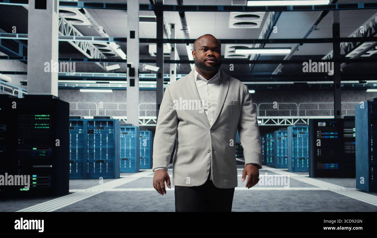 Smiling engineer walking in data center, checking hardware for system stability. Happy employee overseeing server farm, configuring infrastructure to optimize performance, camera A Stock Photo