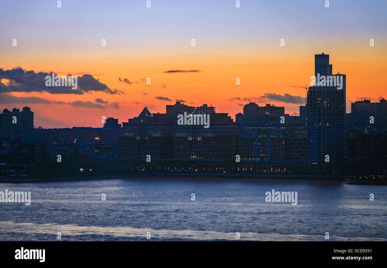 The silhouetted skyline of Jersey City seen from New York City with a dramatic sunset and colorful clouds over the Hudson River in New Jersey, USA Stock Photo