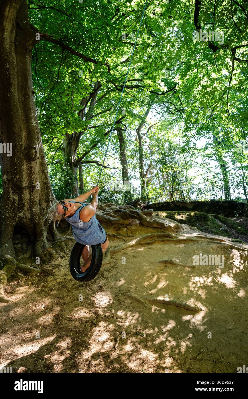 Lady having fun on a rope swing in the forest, lovely light coming ...