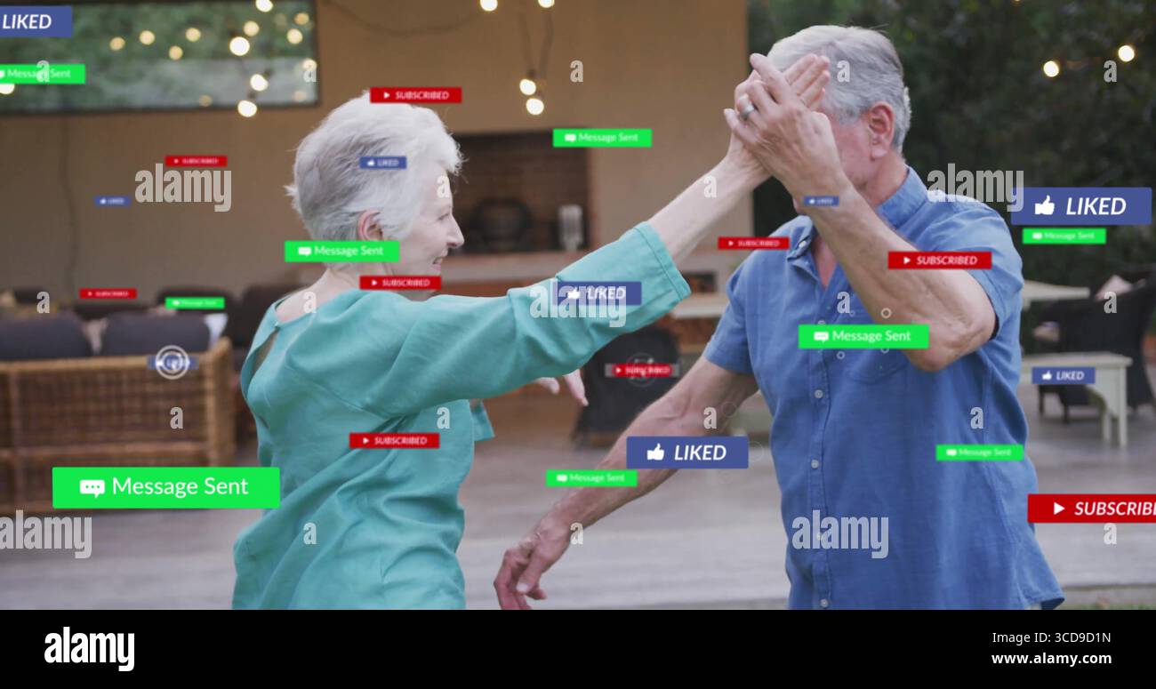 Dancing senior couple exchanging high-five on patio under string lights, with digital notifications Stock Photo
