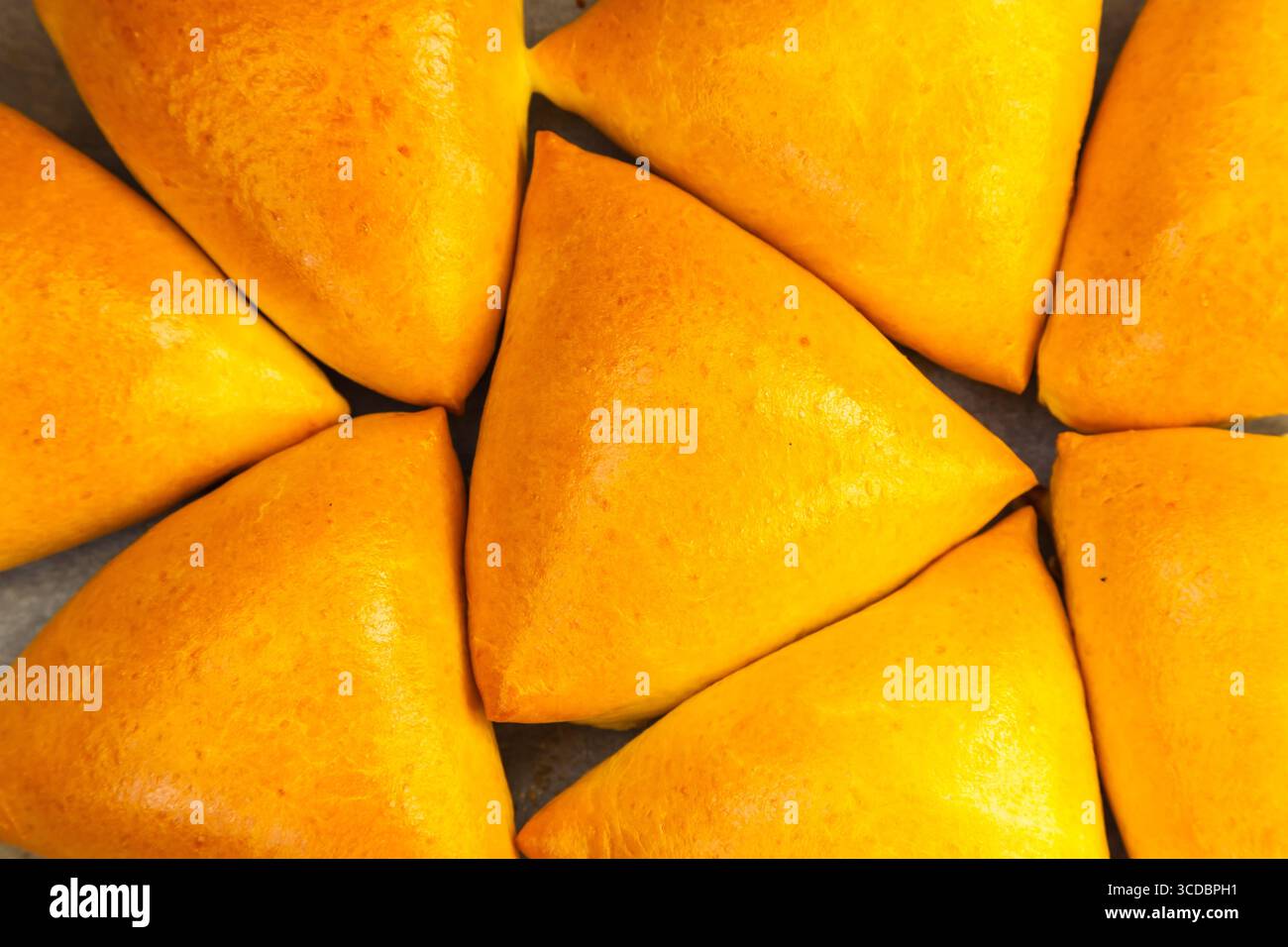 Homemade baked triangular buns lie on white parchment. Stock Photo