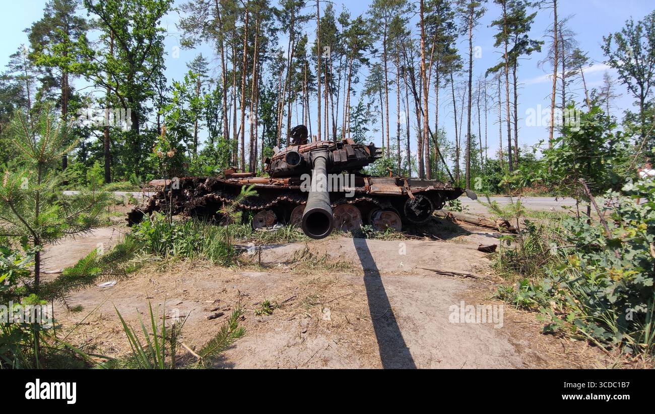 Burnt-out Russian tank with blue-and-yellow Ukrainian flag graffiti, [точне місце], Kyiv Oblast, Ukraine. Photographed on 6 July 2022, aftermath of the 2022 Russian invasion. - Smartphone Captured Stock Image