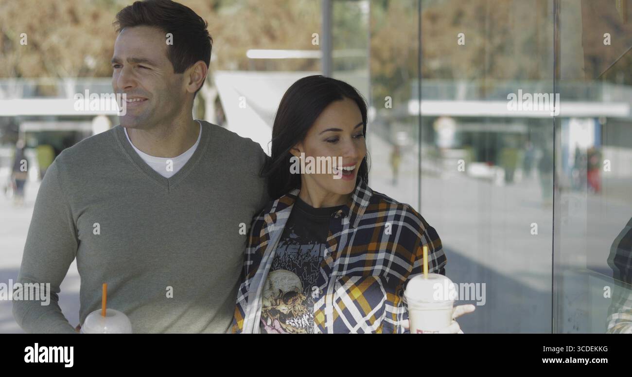 Trendy young woman exclaiming and pointing at merchandise in a store window as she and her boyfriend stroll along enjoying takeaway coffee Stock Photo