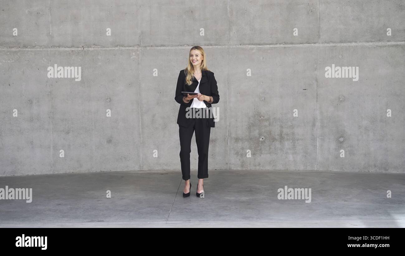 Professional woman in business attire holding a tablet, standing confidently in a contemporary, minimalist office space Stock Photo