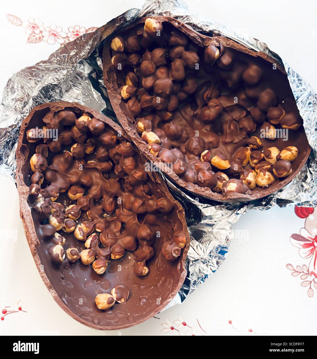 Chocolate Easter egg. Two halves of a chocolate Easter egg filled with hazelnuts on aluminum foil silver background. Easter and holidays. Close-up. Stock Photo